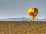 montgolfière jaune et rouge pealz gas survolant un champ agricole avec montagnes en arrière-plan