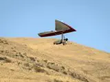 deltaplaniste décollant d'une colline avec voile rouge et blanche sous ciel bleu