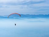 A paraglider soaring above misty mountains under a clear blue sky capturing the essence of adventure and freedom.
